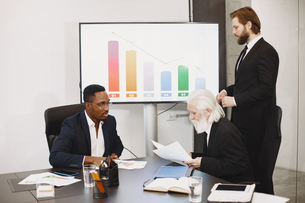 creative-02 Three businessmen discussing financial data in a modern office setting with charts.