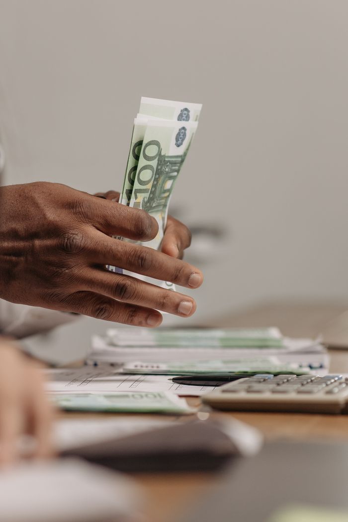 Crafting Captivating Headlines: Your awesome post title goes here Close-up of hands counting US dollar bills on a cluttered desk in an office setting.