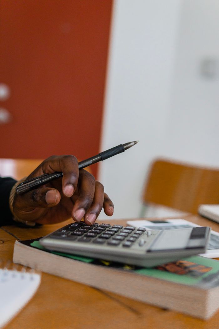 our-story Close-up shot of a hand holding a pen while calculating finances with a calculator on a table.